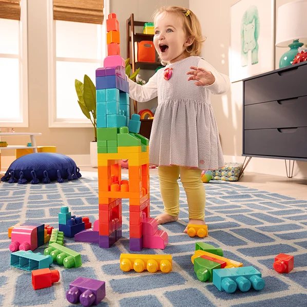 Toddler laughing next to a tall tower of big MEGA Bloks
